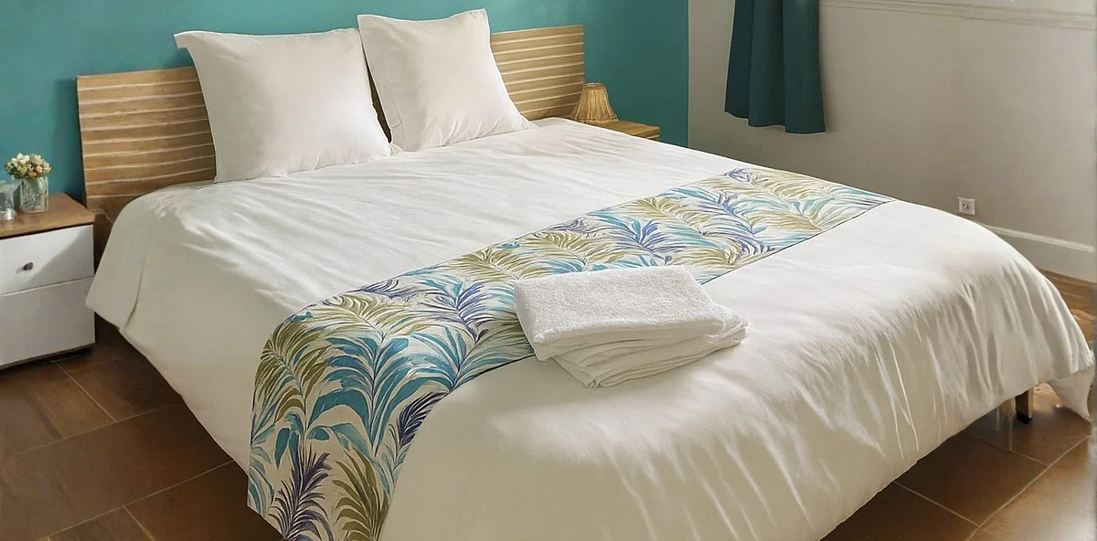Une chambre de la villa : grand lit, linge blanc et jeté aux motifs de feuilles